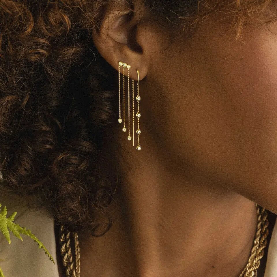 14k gold trio bezel set diamond earrings showcased on a model with curly hair and a stylish look.