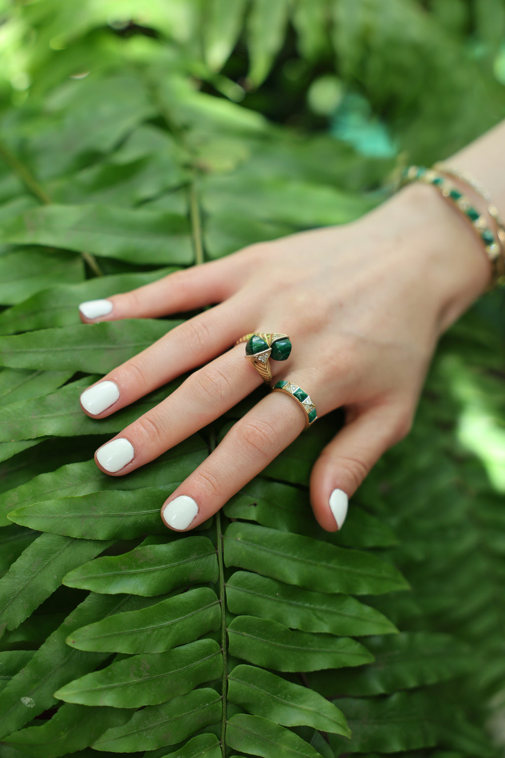 Hand wearing a Bold Artisanal Malachite wrap ring on a green fern, showcasing malachite jewelry ring elegance.