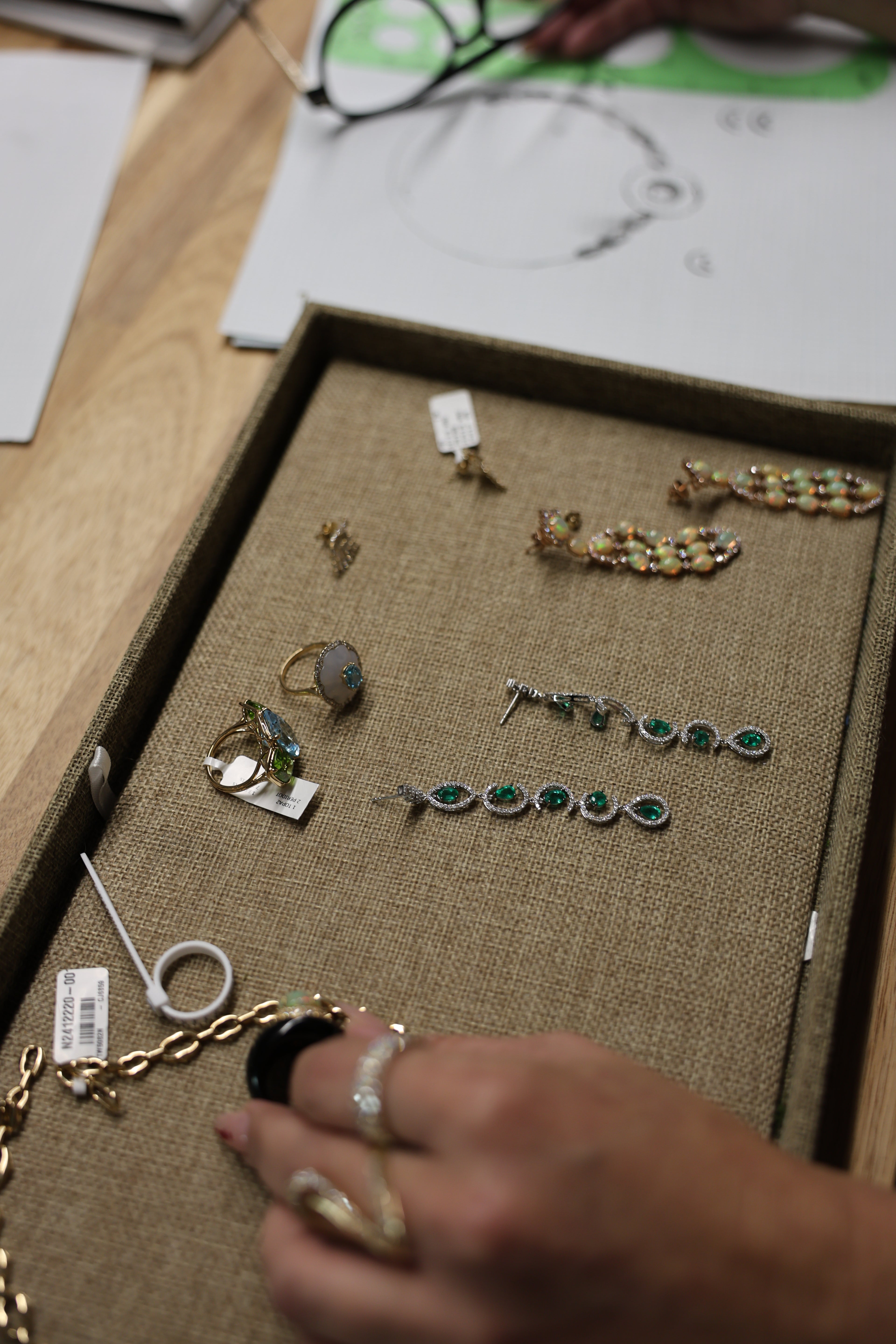 Jewelry set including earrings and necklaces displayed on a textured mat with a hand reaching towards the jewelry.