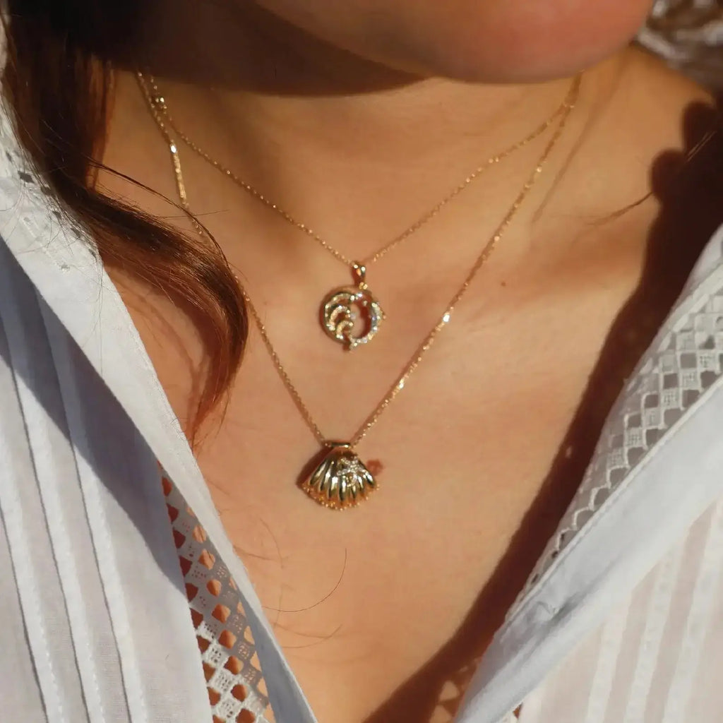Diamond conch shell necklace worn with a starfish pendant, highlighting ocean-inspired jewelry in 14K gold.