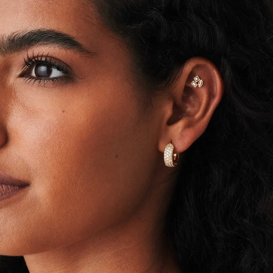 Close-up of a woman wearing baguette diamond earrings and a delicate gold hoop earring.